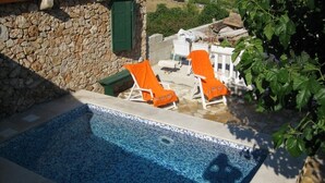 Une piscine avec deux chaises longues et une table, entourée de murs en pierre et de verdure.