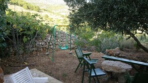 Un espace patio avec un sol en pierre, des chaises vertes, une table et un portique.
