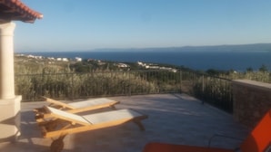Une terrasse avec des chaises longues donnant sur une vue panoramique de la côte.