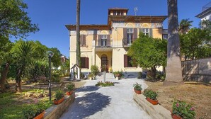 Un edificio a due piani con un ingresso centrale, circondato da un giardino con piante in vaso e un vialetto che conduce all'ingresso.