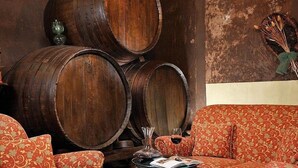 A room with a sofa and chairs, wooden barrels, and a small table with a glass.