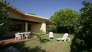 Ein Haus mit einer Terrasse, einem Tisch mit Stühlen und zwei Liegestühlen.