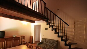 Ein Wohnzimmer mit einer Holztreppe, einem Sofa, einem Esstisch und einem Fernseher.