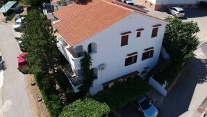 Un edificio blanco con techo de tejas rojas, numerosas ventanas y un estacionamiento con coches.
