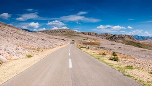 Una larga carretera recta a través de un paisaje árido con terreno rocoso y vegetación escasa.