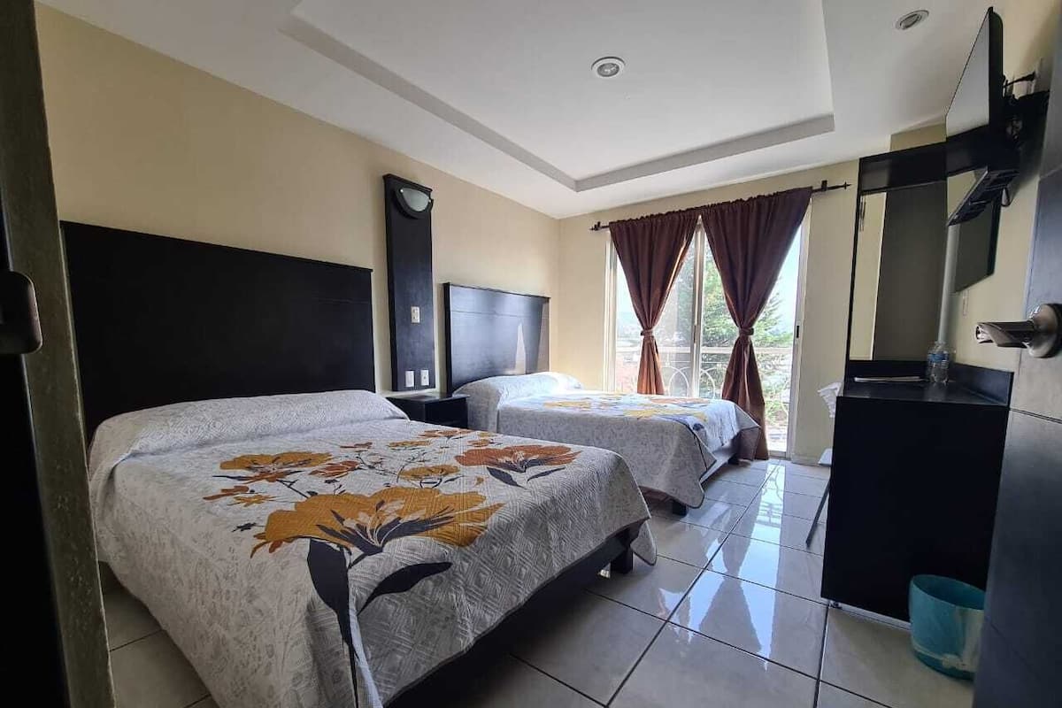 A hotel room with two beds, a TV, a desk, and a window with curtains.