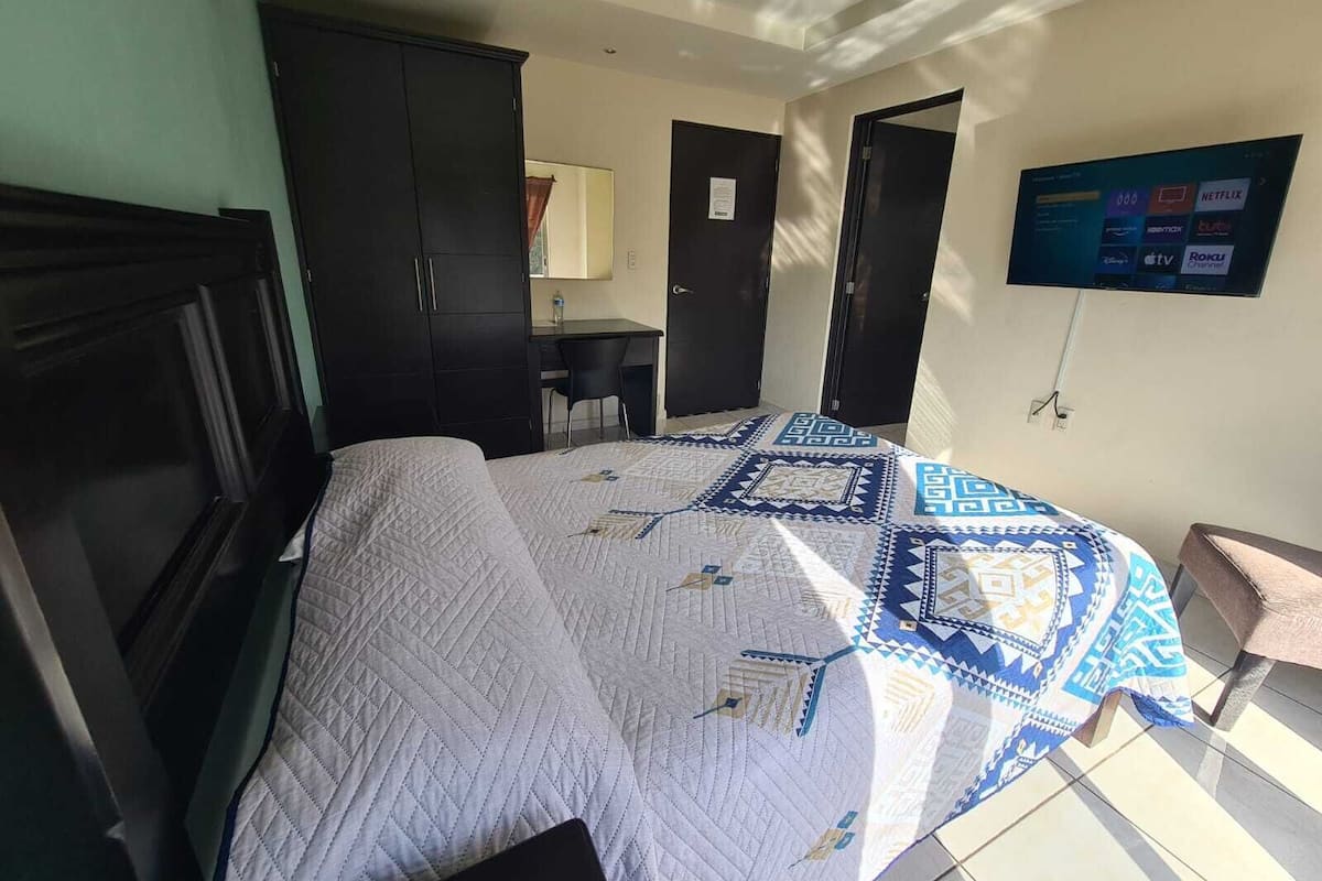 A bedroom with a bed, a desk, and a TV mounted on the wall.