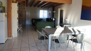 A spacious living area with a high ceiling, a green sofa, a dining table with chairs, and a kitchen area with a refrigerator. - Maison 4 chambres proche plage (023) (Biscarrosse)