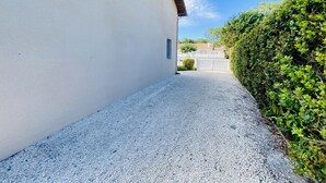 A gravel driveway leading to a white building with a small window and a door. - Maison 4 chambres proche plage (023) (Biscarrosse)
