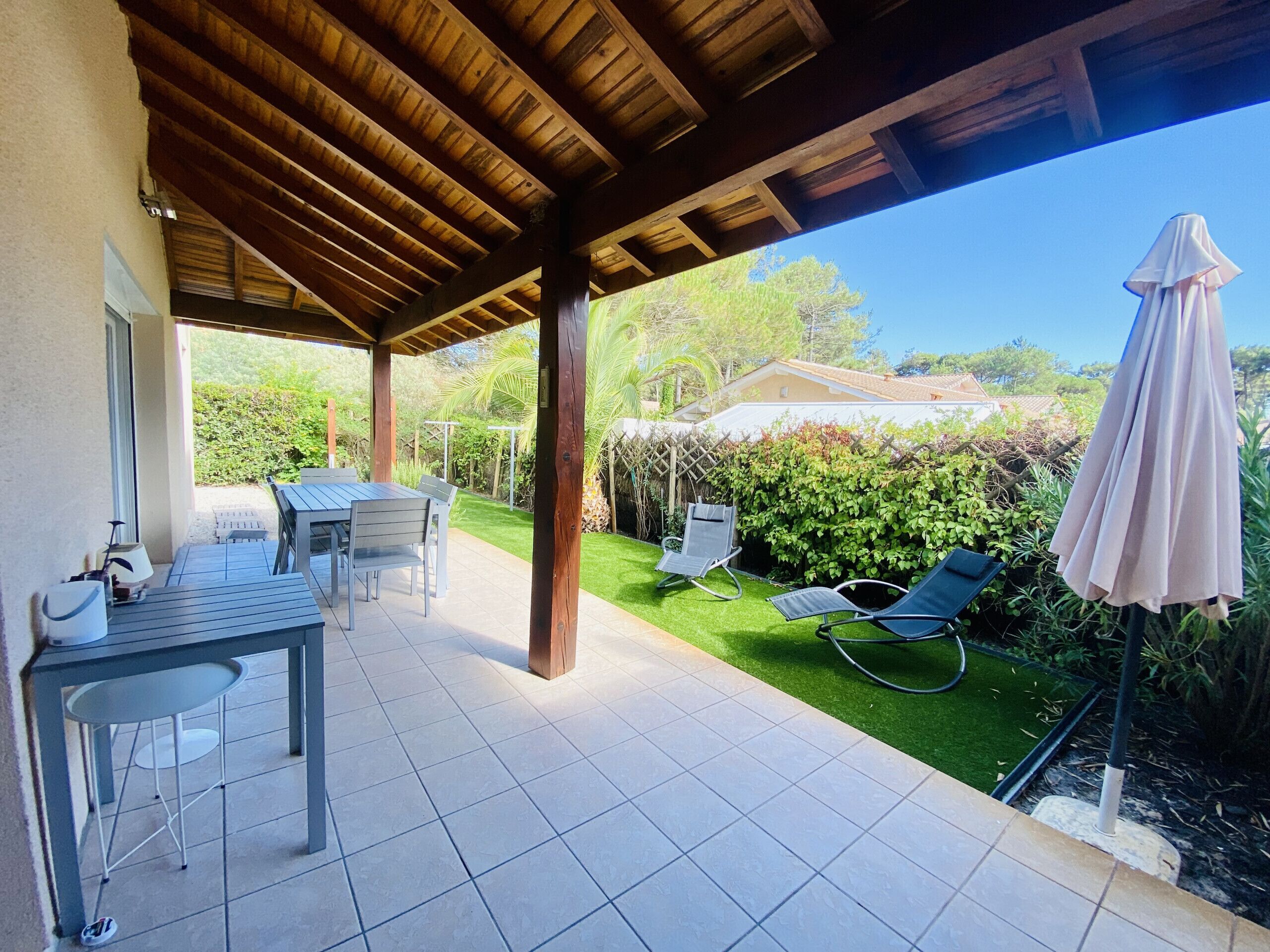 A covered patio area with a table and chairs, a lawn chair, and a covered umbrella.