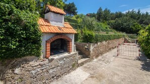 A brick-built outdoor oven with a tiled roof, surrounded by lush greenery and a stone wall. - Apartment in Jelsa with Terrace, Air condition, WIFI (3621-2) (Jelsa)
