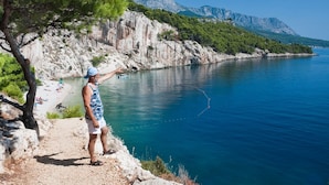 A coastal scene with a rocky path, a beach with people, and a clear blue sea. - Studio apartment in Podaca with Seaview, Terrace, WIFI (3676-2) (Podaca)