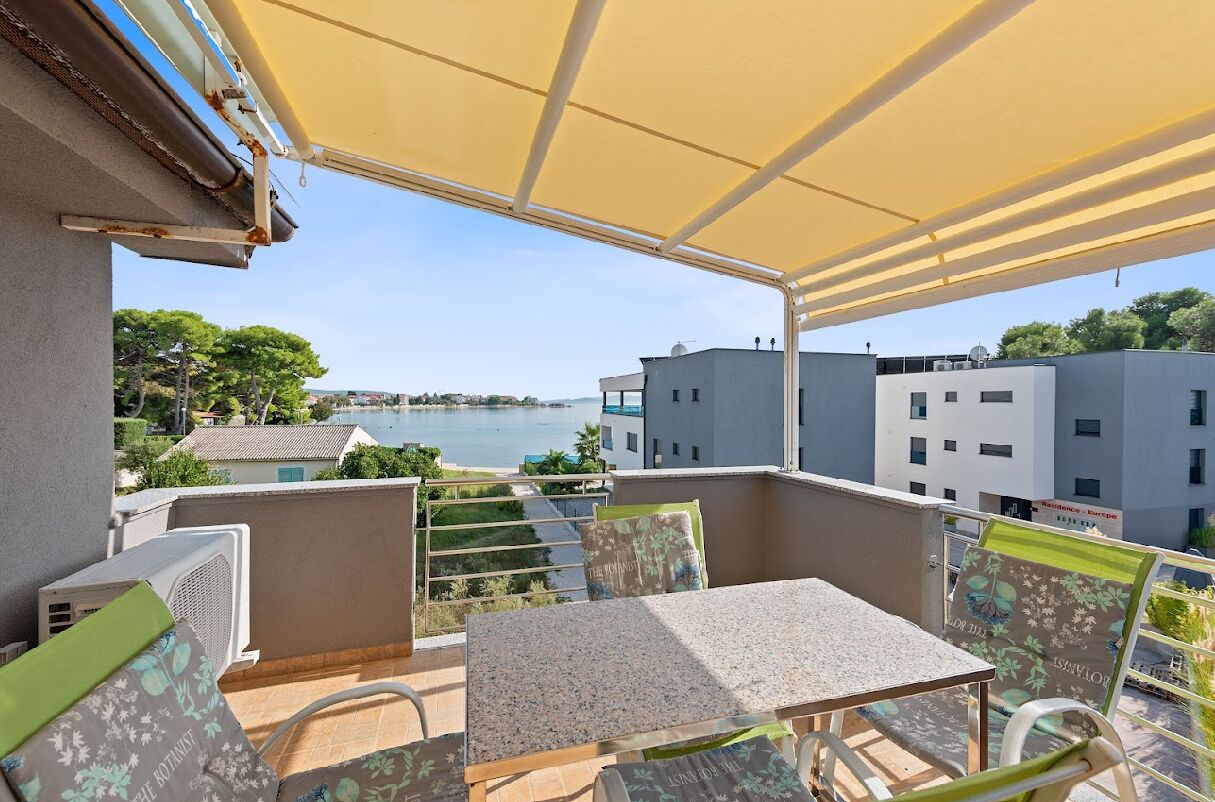 A balcony with a table and chairs, overlooking a body of water and buildings.