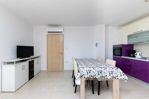 Ein gemütlicher Raum mit Esstisch, Stühlen, einem Fernseher auf einer Kommode, einer Küchenzeile mit violetten Schränken und einer Tür.