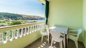 Un balcón con mesa y sillas, con vista a un paisaje costero con edificios y colinas.