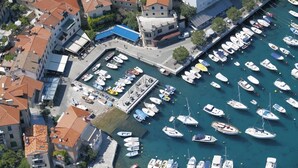 An aerial view of a marina with numerous boats docked, surrounded by buildings with red-tiled roofs.