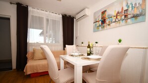 A dining area with a white table set for two, a sofa, and a cityscape painting on the wall.