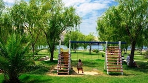 A playground with swings and a slide, surrounded by trees and a body of water.