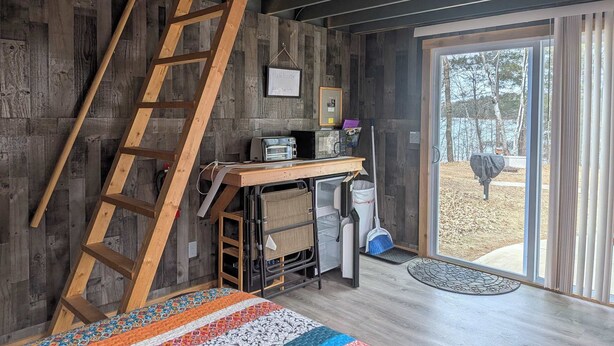 A loft-style room with a wooden ladder, a desk with a toaster, a broom, and a welcome sign.