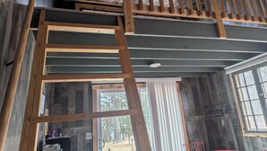 A loft-style room with a wooden ladder, a window with blinds, and a red chair.