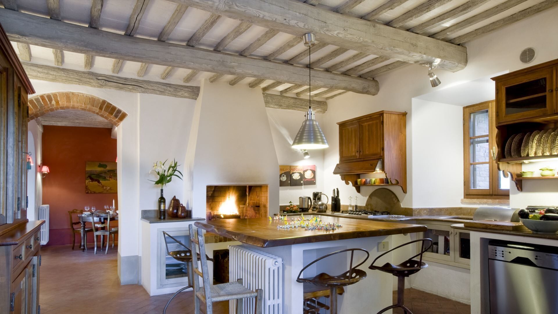 A rustic kitchen with exposed wooden beams, a central island with bar stools, and a dining area with a table and chairs.