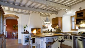 A rustic kitchen with exposed wooden beams, a central island with bar stools, and a dining area with a table and chairs. - Montestigliano, an authentic farmhouse in the heart of Tuscany, is an oasis of peace and beauty that offers its guests refined residences and an enchanting view (Sovicille)