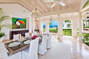 A spacious dining area with a large table set for six, white chairs, and a painting of a toucan on the wall.