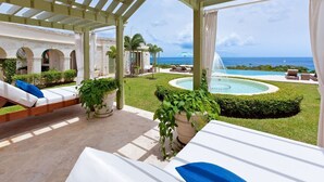Un'area esterna coperta con poltrona relax, piscina e vista sull'oceano.