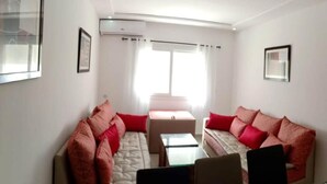 A living room with two sofas, a coffee table, and a TV. There is a window with curtains and an air conditioning unit on the wall. - Beautiful Sea View Apartment in Saidia 4268 (Saidia)