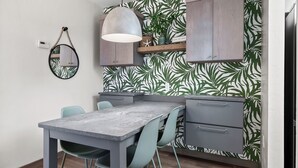 A compact kitchen with a dining table, chairs, a hanging light fixture, and a wall with a leaf pattern. - Cozy Garden View 1 bed, 1 bath at Sanibel Moorings #212 (Sanibel)