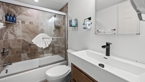 A modern bathroom with a glass-enclosed shower, a white toilet, a sink with a black faucet, and toiletries on a shelf. - Cozy Garden View 1 bed, 1 bath at Sanibel Moorings #212 (Sanibel)