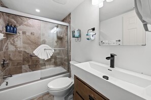 Une salle de bain moderne avec une douche à parois de verre, des toilettes blanches, un meuble-lavabo et des articles de toilette fixés au mur.
