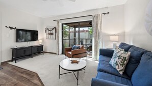 A living room with a TV, sofa, coffee table, and a balcony with a view. - Cozy Garden View 1 bed, 1 bath at Sanibel Moorings #212 (Sanibel)