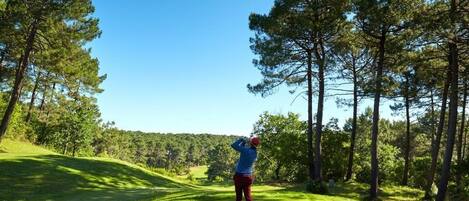 A golf course with a clear sky, trees, and a golfer in mid-swing.