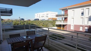 A balcony with a table and chairs, overlooking a street with buildings and greenery. - Magnifique T2 avec terrasse à 50m de la plage (094) (Biscarrosse)