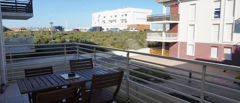 Un balcon avec une table et des chaises, donnant sur un parking et des immeubles.