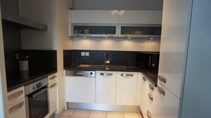 A compact kitchen with white cabinets, a black countertop, a dishwasher, an oven, and a microwave. - Magnifique T2 avec terrasse à 50m de la plage (094) (Biscarrosse)
