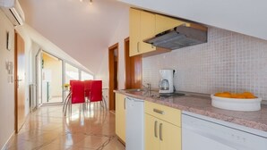 Una cocina moderna con armarios amarillos, un lavavajillas blanco y una cafetera. Hay una silla roja y un cuenco con naranjas en la encimera.