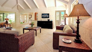 A spacious living area with wicker furniture, a television, and a ceiling fan. - Tropical Villa with Pool Near Beach - Jessamine (Gibbes)