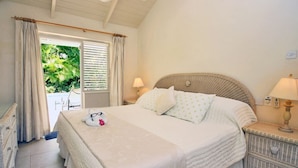 A bedroom with a bed, nightstands, a window with curtains, and a view of greenery outside. - Tropical Villa with Pool Near Beach - Jessamine (Gibbes)