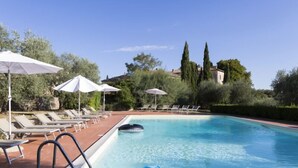 A pool area with lounge chairs and umbrellas, surrounded by greenery and buildings in the background. - Montestigliano, an authentic farmhouse in the heart of Tuscany, is an oasis of peace and beauty that offers its guests refined residences and an enchanting view (Rosia - Sovicille)