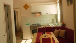 Une cuisine de taille réduite avec des meubles blancs, une table à manger recouverte d’une nappe rouge et un canapé rouge.