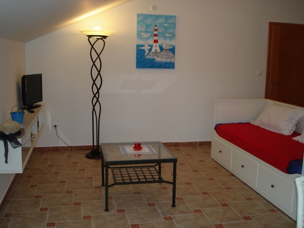 A room with a bed, a small table, a floor lamp, a painting, and a television.