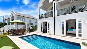 Uma casa de dois andares com piscina, mobiliário de exterior e uma varanda.