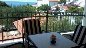 Un balcon avec une table et des chaises, donnant sur une zone côtière avec des maisons et de la végétation.
