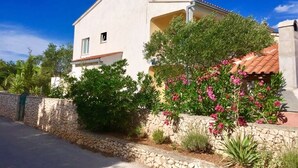 Un bâtiment blanc surmonté d’un toit de tuiles rouges, entouré de murs de pierre et d’une végétation luxuriante.