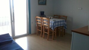 Une pièce comprenant une table à manger, des chaises, un tableau au mur et une fenêtre avec des stores.