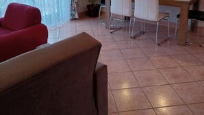 A living room with a red sofa, a brown couch, a dining table with chairs, a potted plant, and a clock on the wall.