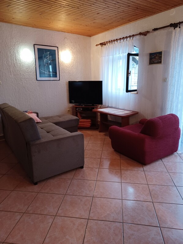 Een woonkamer met een grijze bank, een rode fauteuil, een televisie en een kleine tafel.