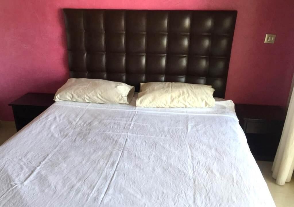 A bed with a dark headboard and two pillows, set against a pink wall.
